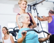 Senior woman doing back training with trainer in gym