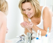 Young happy woman washing face with water standing in bathroom